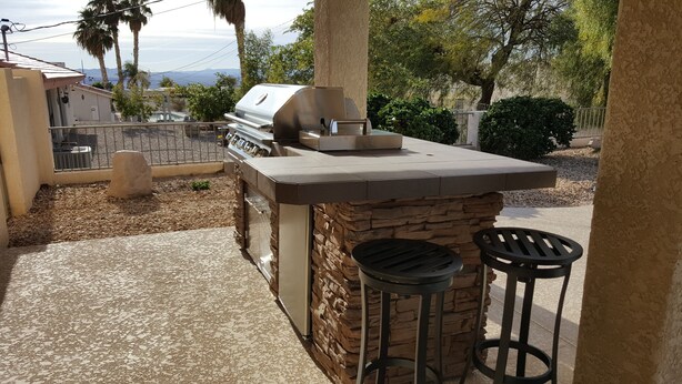 An outdoor kitchen with a grill, stone accents, and two stools. - Clean 3 Bed/2 bath home w/ pool, BBQ & covered patio, locked RV & boat parking (Lake Havasu City)