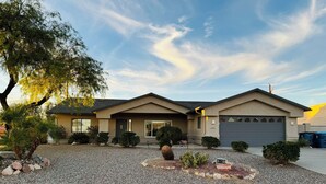 A two-story house with a gravel driveway, a garage, and a well-maintained lawn with various plants. - Clean 3 Bed/2 bath home w/ pool, BBQ & covered patio, locked RV & boat parking (Lake Havasu City)