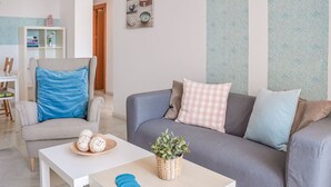 Un salon moderne avec un canapé gris, une table basse blanche et un fauteuil bleu. On aperçoit une petite plante sur la table basse et un objet décoratif sur le canapé.
