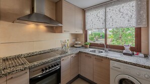 Une cuisine moderne dotée de plans de travail en granit, d’appareils électroménagers en acier inoxydable et d’une fenêtre agrémentée de rideaux à motifs.