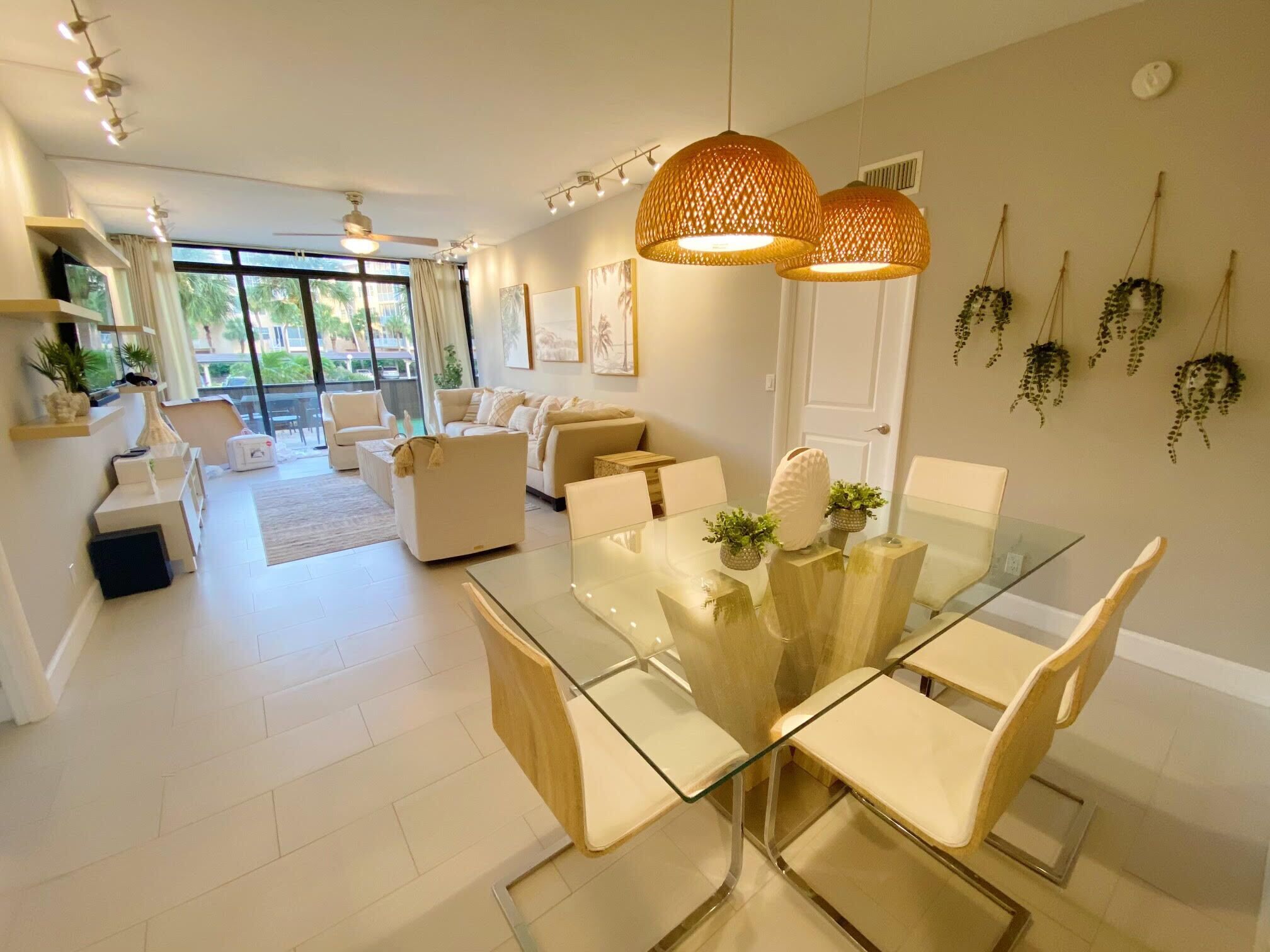A modern living room with a glass dining table, beige sofas, and a ceiling fan.