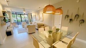 Uma sala de estar moderna com uma mesa de jantar de vidro, sofás bege e um ventilador de teto.