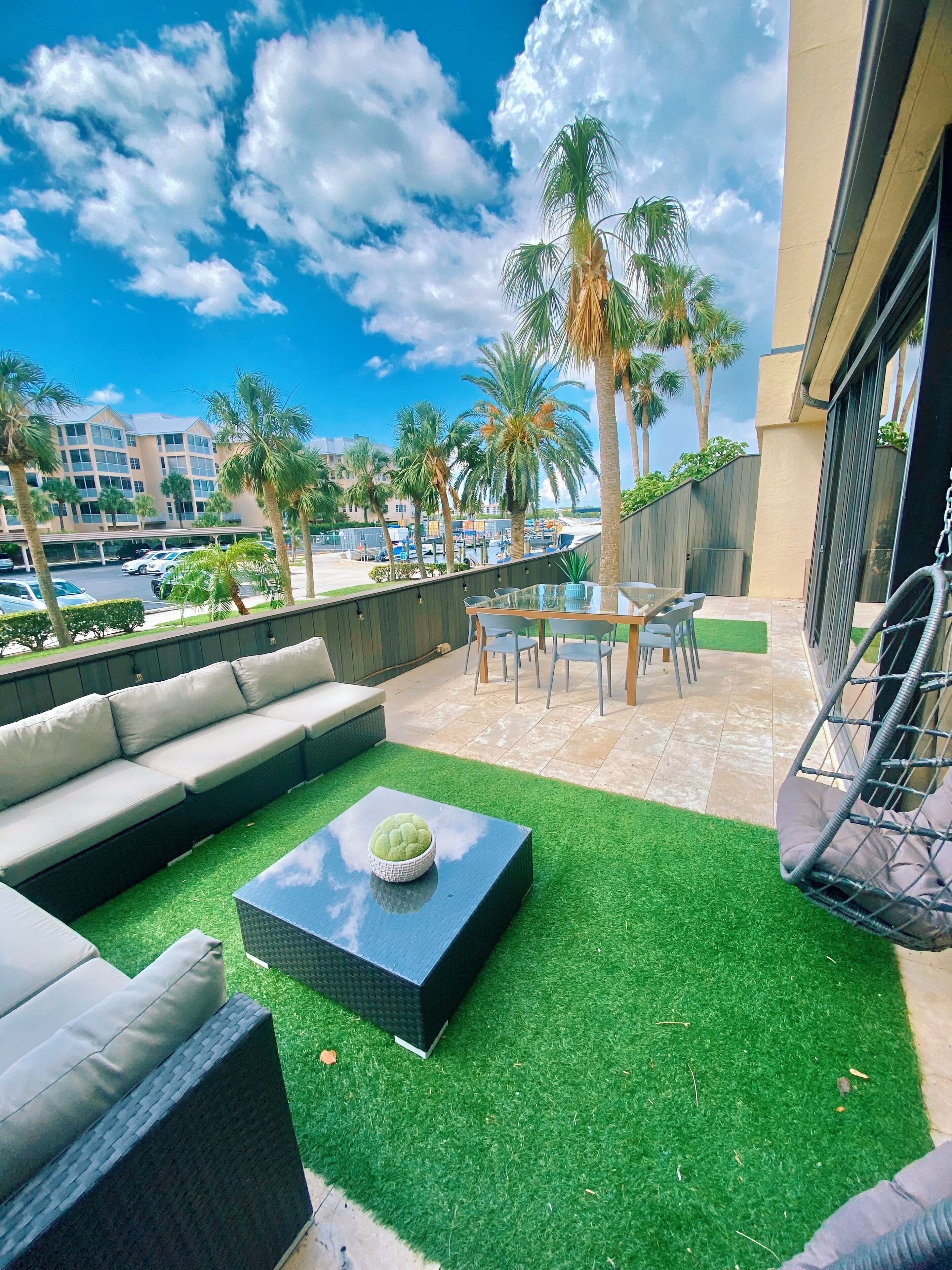 Un patio en la azotea con un sofá, una mesa y sillas. Se ven palmeras y una vista de un edificio de hotel al fondo.