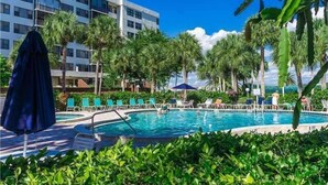 Piscina com espreguiçadeiras e palmeiras, cercada por um edifício com varandas.
