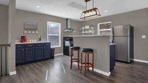 A modern kitchen with dark blue cabinets, a central island with stools, a stainless steel refrigerator, and a pendant light. - The Bittersweet Inn: Brand new 6 bed 5 bath house (Hermann)