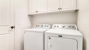 A laundry room with two white appliances, a door, and white cabinets. - 🏖️Mauna Lani Townhome with Private Beach Club Access | Kulalani 404 (Kamuela)