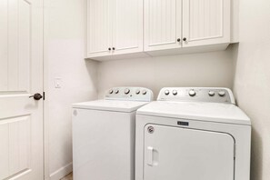 A laundry room with two white appliances, a door, and white cabinets. - 🏖️Mauna Lani Townhome with Private Beach Club Access | Kulalani 404 (Kamuela)