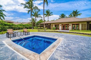 A swimming pool with lounge chairs, palm trees, and a building with a tiled roof.