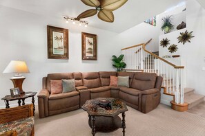 A living room with a sectional sofa, a coffee table, a lamp, and a staircase with a sign. - 🏖️Mauna Lani Townhome with Private Beach Club Access | Kulalani 404 (Kamuela)