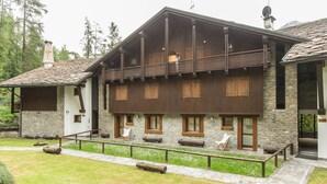A two-story wooden house with stone walls, a balcony, and a stone pathway leading to the entrance.
