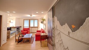 A living room with a red sofa, a wooden coffee table, and a large painting of a mountain landscape.