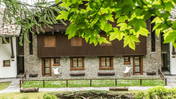 A traditional building with stone walls and wooden shutters, featuring a covered outdoor seating area with chairs.