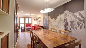A dining area with a wooden table and chairs, a red sofa, and a wall mural of a mountain scene.