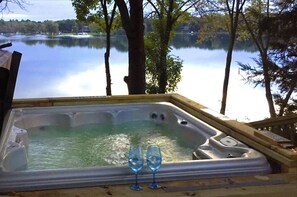 Un bain à remous avec deux verres d’eau, entouré d’arbres et offrant une vue sur le lac.