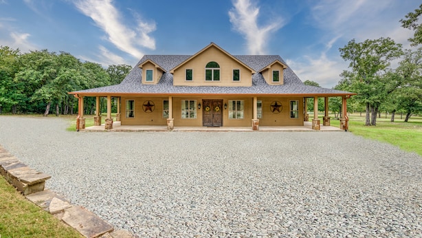 A large, two-story house with a covered porch, a gravel driveway, and a landscaped lawn. - Lone Star State of Mind - 6BD/5BA w/ FIshing Pond & Fully Furnished Kitchen (Sherman)