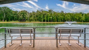A wooden dock with metal railings and benches, overlooking a lake with a fountain and dense trees in the background. - Lone Star State of Mind - 6BD/5BA w/ FIshing Pond & Fully Furnished Kitchen (Sherman)