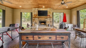 A rustic cabin with a stone fireplace, wooden ceiling, and large windows overlooking a wooded area. - Lone Star State of Mind - 6BD/5BA w/ FIshing Pond & Fully Furnished Kitchen (Sherman)
