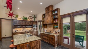 A kitchen with wooden cabinetry, granite countertops, and a large island. There are bar stools and a dining table visible. - Lone Star State of Mind - 6BD/5BA w/ FIshing Pond & Fully Furnished Kitchen (Sherman)