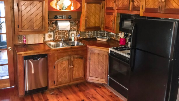 Una cocina con armarios de madera, lavavajillas de acero inoxidable, refrigerador negro y microondas.