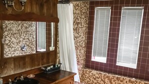 Un baño con tocador de madera, lavamanos, espejo y ventana con persianas.