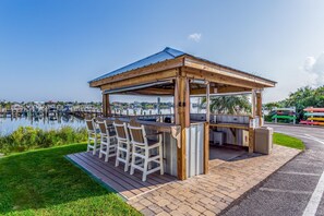A wooden gazebo with a metal roof, a bar area with chairs, and a view of a marina with boats.