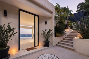 Een modern gebouw met een glazen deur die leidt naar een balkon met uitzicht op zee, met potplanten en een trap.