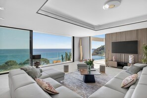Een moderne woonkamer met een grote televisie, comfortabele zithoek en uitzicht op de oceaan.