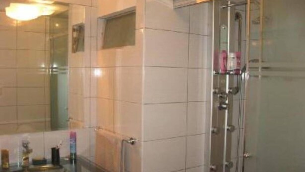 Casa de banho com cabine de chuveiro em vidro, lavatório com espelho e chão em azulejo.