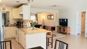 A modern kitchen with a central island, a dining area with chairs, a television, and a living room with a sofa.