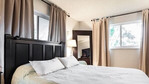A hotel room with a large bed, dark headboard, and beige curtains.