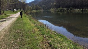 Un sentier paisible au bord du lac, où l’on voit une personne se promener, entourée d’une végétation luxuriante et de collines.