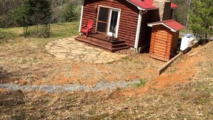Une petite cabane avec un toit rouge, une véranda dotée d’un fauteuil Adirondack rouge et un chemin de pierres menant à l’entrée.