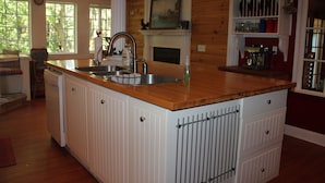 A kitchen with a wooden countertop, white cabinetry, a sink, and a fireplace. - Cozy, Family Friendly Log Cabin Close To Everything! (Williams Bay)