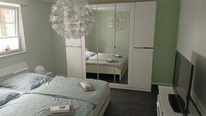 Une chambre à coucher moderne, équipée d’un lit, d’une armoire, d’un téléviseur et d’un lustre original.