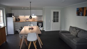 Une cuisine moderne avec des meubles blancs, une table à manger avec des chaises, un canapé gris et un tableau accroché au mur.