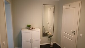 Un couloir avec une armoire blanche, un miroir et une porte.