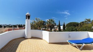 Une terrasse sur le toit avec un mur blanc, une chaise longue bleue et une cheminée blanche.