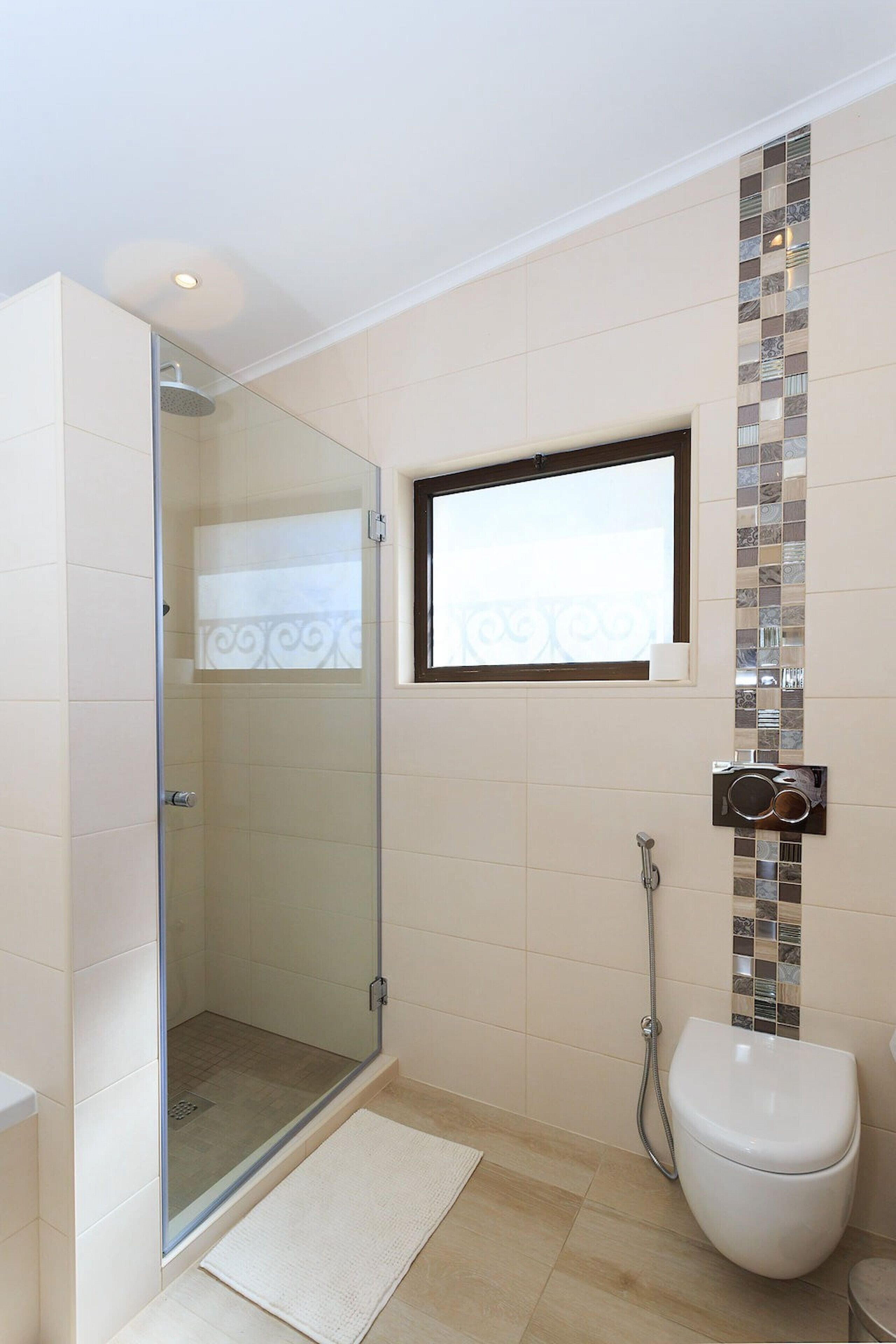 A modern bathroom with a glass shower enclosure, a toilet, and a small window.