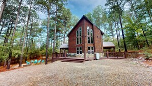 A wooden cabin with a deck, surrounded by trees. - Yellow Rose Cabin: Pet-Friendly Hochatown Getaway (sleeps 12) w/ Hot Tub, Arcade (Broken Bow)