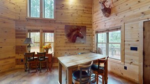 A wooden cabin interior with a dining table, chairs, a lamp, and a deer head mounted on the wall. - Yellow Rose Cabin: Pet-Friendly Hochatown Getaway (sleeps 12) w/ Hot Tub, Arcade (Broken Bow)