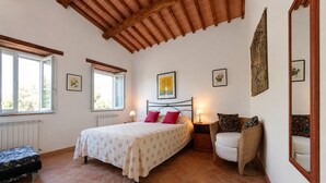 Un dormitorio con cama, dos mesitas de noche, una silla, un radiador y una ventana.