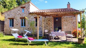 Una casa de piedra con techo de tejas, un porche cubierto con mobiliario exterior y un jardín.