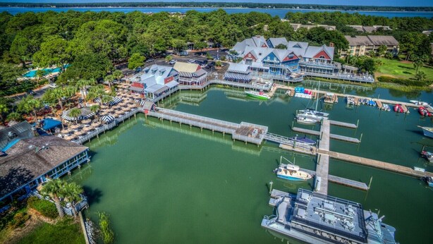An aerial view of a marina with boats docked, a pier, and a building with a blue roof.