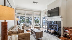 A spacious living room with a fireplace, large windows, and a flat-screen TV.