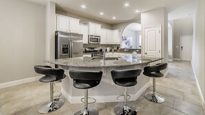 A modern kitchen with a central island, stainless steel appliances, and bar stools.