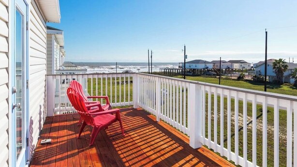 A wooden deck with a white railing, a red chair, and a view of the ocean. - Phoenix Rising - Chill Beach Vibes, 4 Decks! (Surfside Beach)