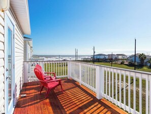 Une terrasse en bois avec une balustrade blanche, une chaise rouge et une vue sur l’océan.