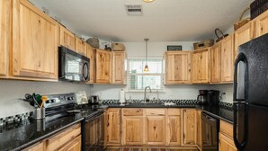 A kitchen with wooden cabinets, a black refrigerator, a microwave, and a stove. - Phoenix Rising - Chill Beach Vibes, 4 Decks! (Surfside Beach)
