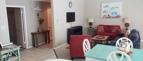 A living room with a red sofa, a blue table, and a TV mounted on the wall.