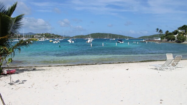 Una playa de arena blanca, algunas sillas de playa y varios barcos en el agua.